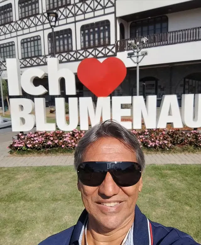 Solivam de óculos escuros e camisa azul, sorrindo, em frente ao letreiro "Ich liebe Blumenau", numa excursão ao Sul do Brasil.