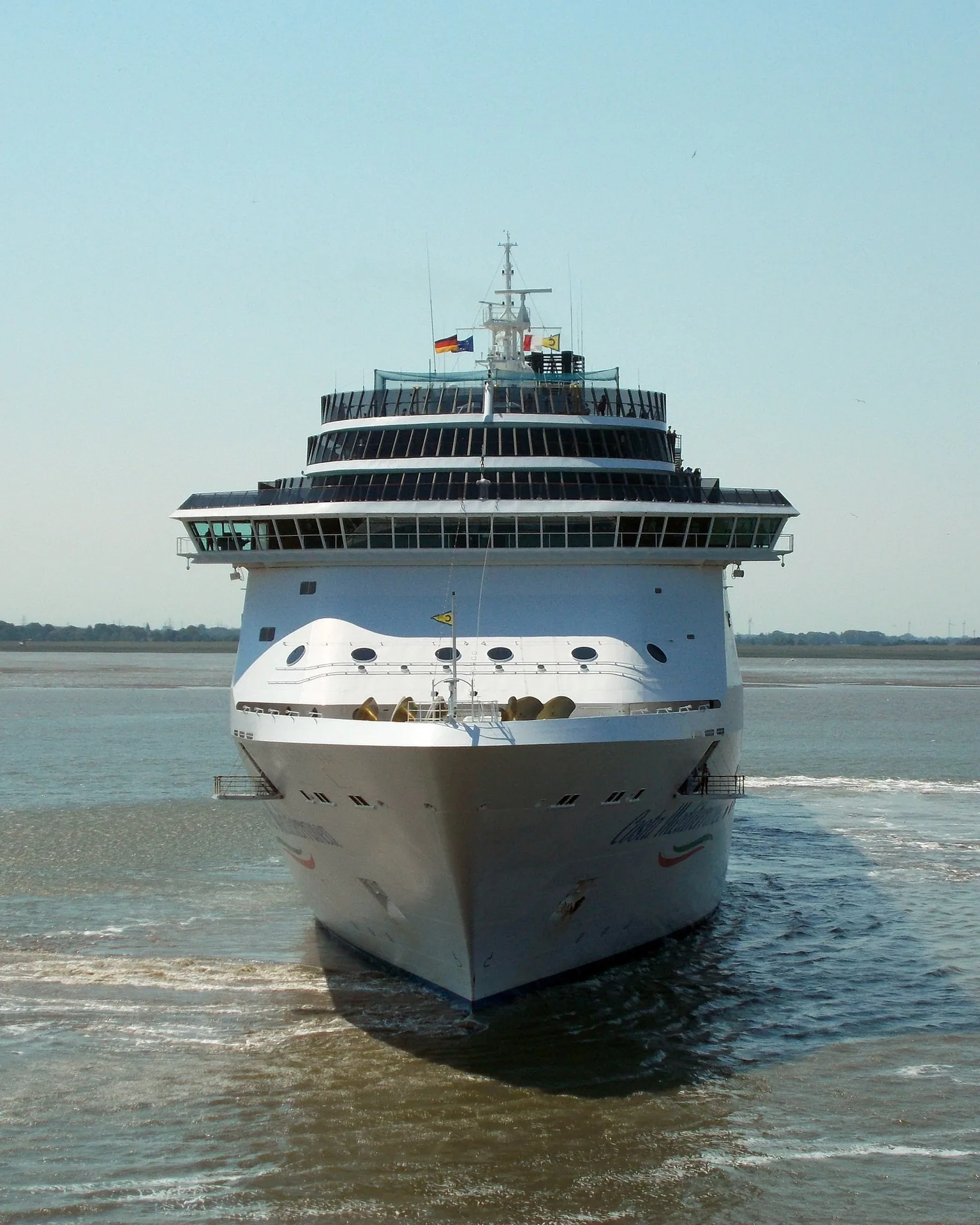 Navio de cruzeiro branco visto de frente, navegando em águas calmas.