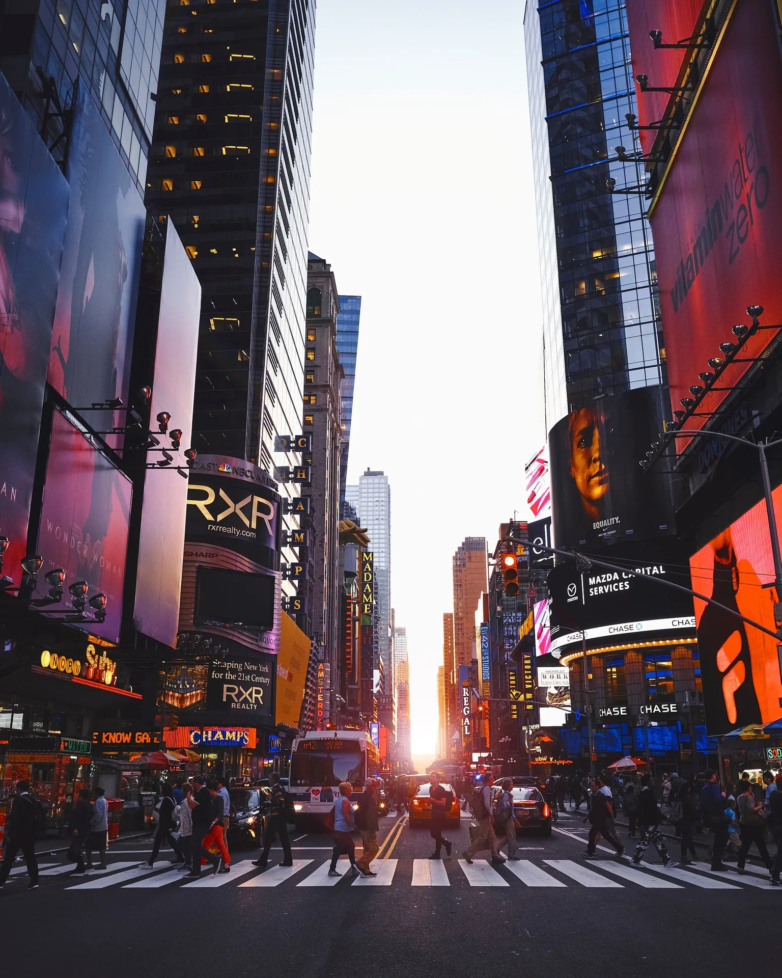 Times Square, em Nova York, ao pôr do sol, com painéis luminosos e pedestres na faixa.